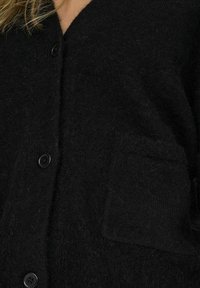 Cardigan nero lavorato a maglia con scollo a V, caratterizzato da una finitura testurizzata, quattro bottoni e una tasca a toppa sul lato anteriore.