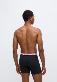 Μαύρα boxer εσώρουχα με αντίθετη λευκή και ροζ μέση που φέρει το λογότυπο της Nike, εμφανιζόμενα από πίσω σε ουδέτερο φόντο.