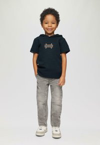 Korte mouw marineblauwe hoodie met de tekst "CALM AND EASY", gecombineerd met lichtgrijze jeans en witte sneakers, staand tegen een neutrale achtergrond.