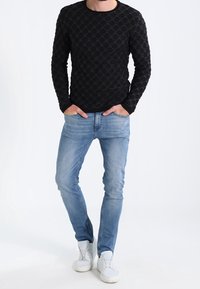 Chemise noire à manches longues avec motif circulaire texturé, associée à un jean slim fit bleu clair et des baskets blanches.