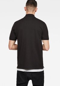 Mustapohjainen lyhythihainen polo paita, jossa on litteä kaulus, sileä rakenne ja hillitty helma. Ei näkyviä logoja tai kuvioita.