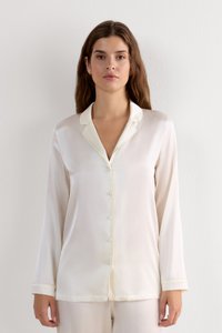 Blusa de seda blanca con cuello, mangas largas y cierre de botones en el frente. Presenta una textura suave y un brillo sutil.