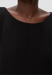 Svart plisserad klänning med en bred, rundad halsringning. Tyget har en strukturerad yta med vertikala linjer. Närbild av den övre delen.