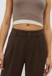 Brązowe spodni w kant z płaskim przodem, przeszytymi bocznymi kieszeniami i pojedynczym zapięciem na guzik. Gładki materiał o ustrukturyzowanym kroju.