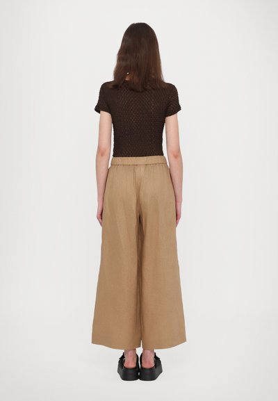 Brązowy dzianinowy top z krótkimi rękawami, połączony z beżowymi spodniami szerokimi w nogawkach i czarnymi butami na platformie, widok z tyłu.