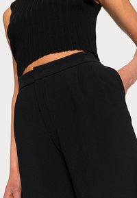 Top corto in maglia ribbed nera abbinato a pantaloni neri a vita alta, con linee pulite e una morbida texture del tessuto per garantire comfort.