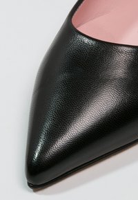 Zapato de punta negro de cuero con un acabado brillante y superficie texturizada, con un interior rosa. Silueta elegante y diseño minimalista.