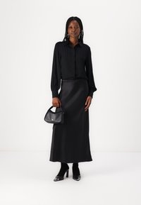 Black, textured blouse with long sleeves and button closure; flowing black satin maxi skirt; small black handbag; heeled shoes.