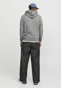 Grauer Kapuzenpullover mit relaxter Passform, kombiniert mit lockeren, dunklen Jeans. Das Outfit wird durch eine hellblaue Mütze ergänzt.