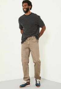 Navy striped short-sleeve t-shirt paired with light brown straight-leg jeans and blue sneakers with orange accents. Plain background.