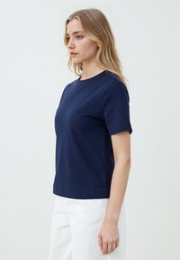 T-shirt in cotone blu navy con maniche corte e scollatura tonda. Il tessuto appare liscio con una vestibilità classica, indossato con pantaloni bianchi.