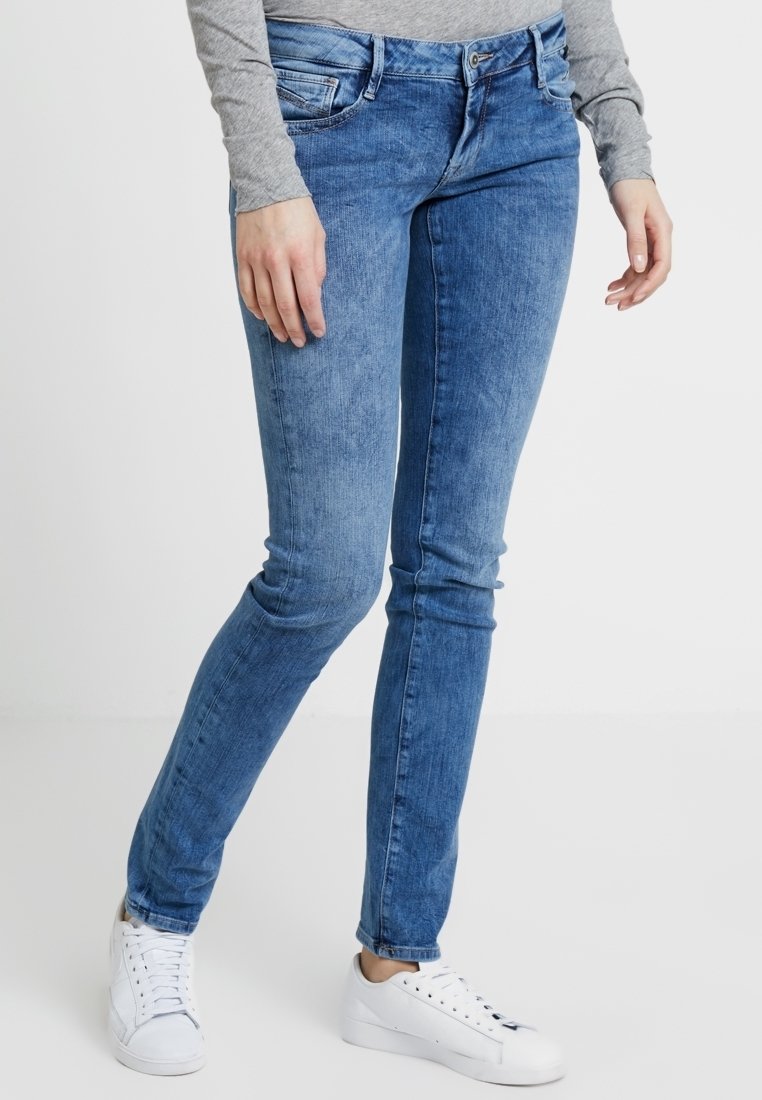 Hubené džíny ve světle modrém denimovém provedení se zesvětleným vzorem. Mají pět kapes, zipový patent a úzký střih. Kombinované s bílými teniskami.