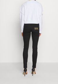 Svarta jeans med en smal passform, utrustade med bakfickor och "VERSACE JEAN COUTURE" broderat i guld. Matchas med en kortärmad vit sweatshirt.