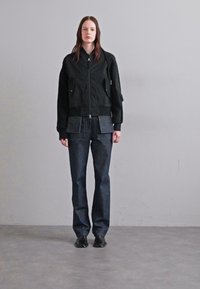 Fekete bomber dzseki, fényes cipzárral, texturált anyagból, elülső zsebekkel, sötét farmernadrággal párosítva, amelyen felvarrt zsebek találhatók, és egyenes fazonú.