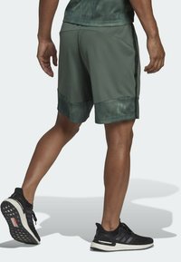 Man som går, iklädd gröna sportshorts med svarta sidostråk och svarta löparskor med vita sulor.