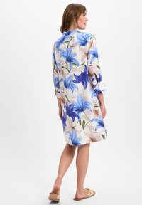 Blumenkleid aus Leinen mit blauen und rosa Lilienmustern, Dreiviertelärmel und einer lockeren Passform, mit einem Rückeneinsatz und seitlichen Schlitz.