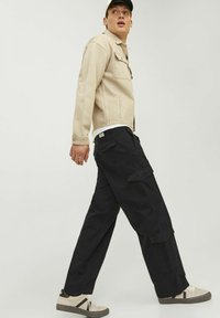 Jachetă din denim bej cu închidere cu nasturi, pantaloni cargo negri cu buzunare și adidași bej cu talpă închisă. Design minimalist, culori neutre.