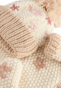 Strik-hat og handsker sæt i creme og beige, med et struktureret ribbet design og blomsterbroderi samt en fluffy pom-pom på hatten.