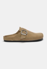 Barna velúr slip-on klumpa, kerek orral, állítható csatpánttal és texturált gumitalppal a tapadásért. Simább felület és minimális varrási részletek.