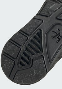 Melna gumijas sporta apavu zole ar teksturētām virsmām, rieviņām un logo. Dizains ietver segmentētas daļas saķerei un elastībai.