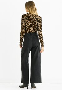 Leopard print long-sleeve top paired with high-waisted, wide-leg black jeans and green heels. The outfit features a fitted silhouette and textured fabric.