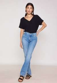 Top nero a V, jeans svasati blu chiaro con design a cinque tasche e sandali neri con accentuazione a fibbia. Tessuto morbido, vestibilità rilassata.