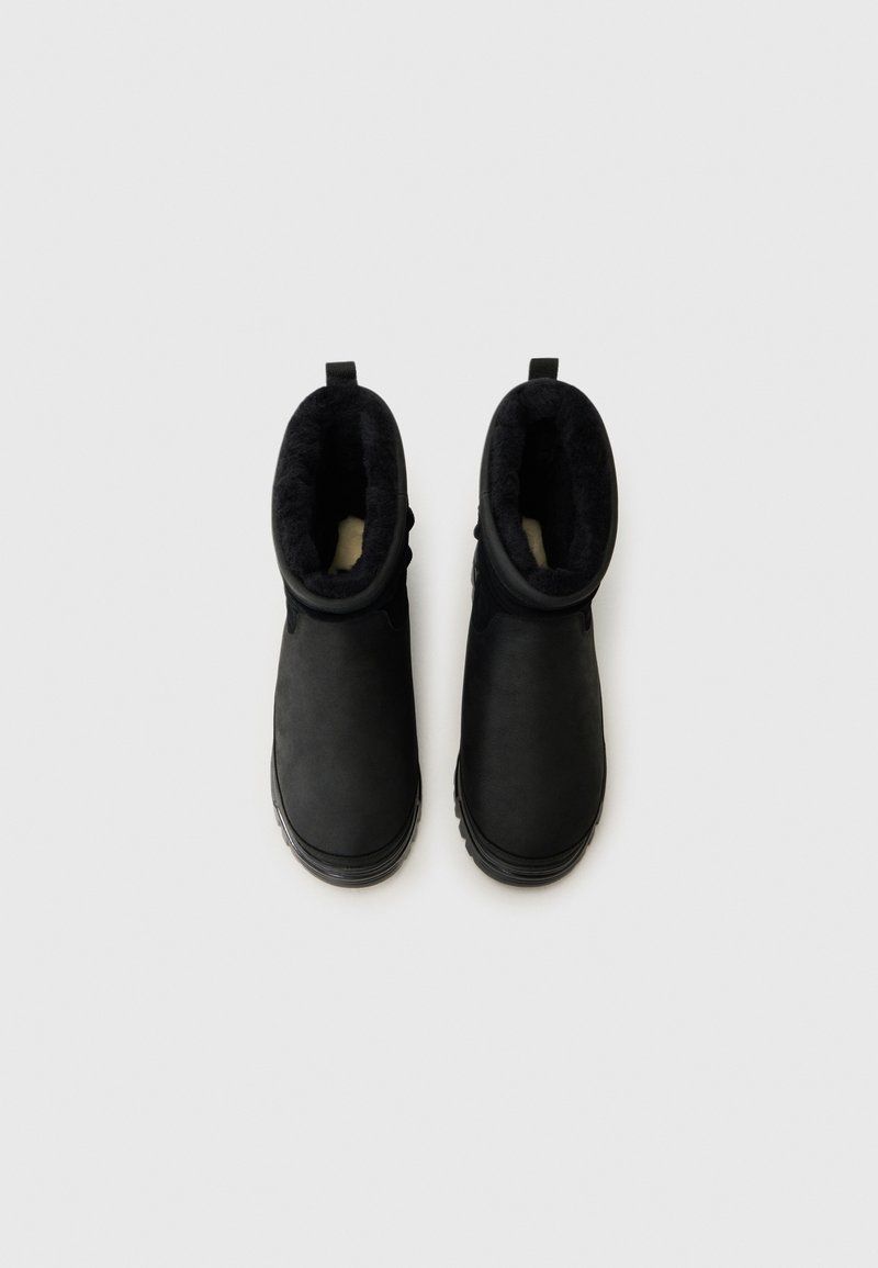 Schwarze Winterstiefel mit einem weichen Futter, von oben auf einem hellen Hintergrund gezeigt. Die Stiefel verfügen über eine Zuglasche und strukturierte Sohlen.