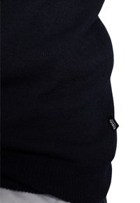 Granatowy sweter wykonany na drutach, z strukturalnym ribbed, z małą czarną metką z napisem "DRD" po lewej stronie, blisko dołu.