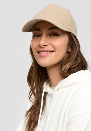 Beige honkbalpet met gestikte details, gedragen door een persoon in een witte hoodie. De pet heeft een gebogen klep en een gestructureerde stof.