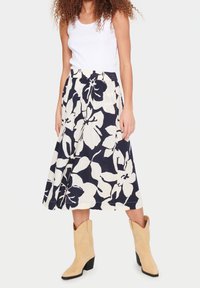 Blommig midikjol i marinblått och krämvitt, med texturerat tyg, elastisk midjeband och en utsvängd silhuett. Kombinerad med beige cowboyboots.