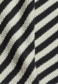 Stickad tyg med en texturerad yta som har diagonala ränder i svart och krämfärgat, sid sömmar med kontrasterande sömnad.