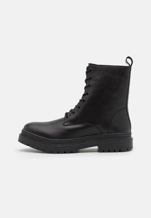 Bottes de combat en cuir noir avec un bout rond, un design à lacets, et une semelle en caoutchouc épaisse avec des crampons profonds pour une meilleure traction.