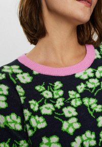 Granatowy sweter z zielono-białymi wzorami kwiatowymi, z różowym prążkowanym kołnierzem. Widok z bliska podkreśla fakturę i szczegóły wzoru.