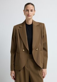 Ruskea kaksinkertainen bleiseri, joka on valmistettu sile�ästä kankaasta. Siinä on näyttävät olkatyynyt, kultasävyiset napit ja sivutaskut, ja se on yhdistetty mustaan yläosaan.