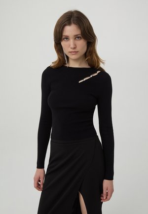 Maglietta nera a maniche lunghe con righe, caratterizzata da un taglio con dettagli decorativi. Il design aderente si abbina a una gonna nera con uno spacco a coscia.