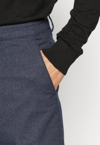 Mörkblå byxor med texturerat tyg, med en sidoficka och dragsko i midjan, parat med en svart långärmad skjorta.