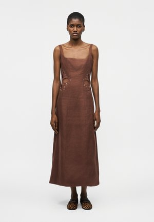 Donna che indossa un abito midi marrone senza maniche con spaccature laterali e dettagli a occhiello, abbinato a scarpe slip-on con stampa leopardata.