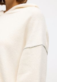Cream-colored hoodie made of soft fabric, featuring a hood, relaxed fit, and contrasting stitching along the sleeves.