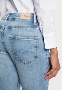 Světle modré džíny z denimu mají středně vysoký pas, koženou zadní nášivku s nápisem "Pepe Jeans" a jednu zadní kapsu se vzorem vlnovky sešitou steháním.