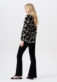 Czarna bluzka w kremowy wzór z długim rękawem i bufkami na ramionach, zestawiona z czarnymi spodniami w stylu dzwonów oraz czarnymi płaskimi sandałami.