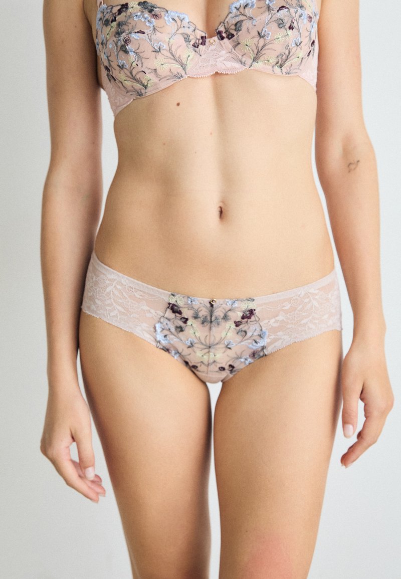 Lace-BH und passende Slips mit floralem Stickmuster in Pastellfarben auf einem transparenten pinken Grund, die filigrane Muster und sanfte Texturen betonen.