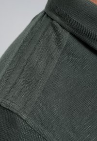 Donkergroene, gestructureerde stof met ribbelaccenten en gladde gedeeltes, die een combinatie van stijlen en materialen toont.
