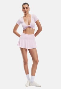 Lys pink crop top med snoet front og korte ærmer, parret med en matchende flared mini nederdel. Glat, strækbart stof med en blød tekstur.