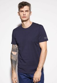 Granatowa koszulka z krótkim r ękawem wykonana z bawełny, z okrągłym dekoltem i subtelnym detalem logo na lewym rękawie.