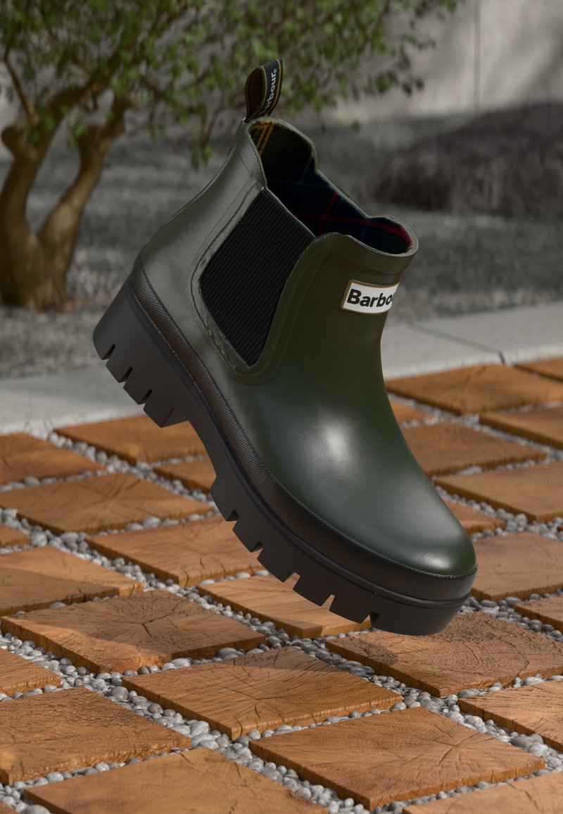 Bota de chuva verde com acabamento brilhante, painéis laterais elásticos, sola preta robusta e forro de padrão xadrez. Apresenta uma alça para facilitar o calçar.