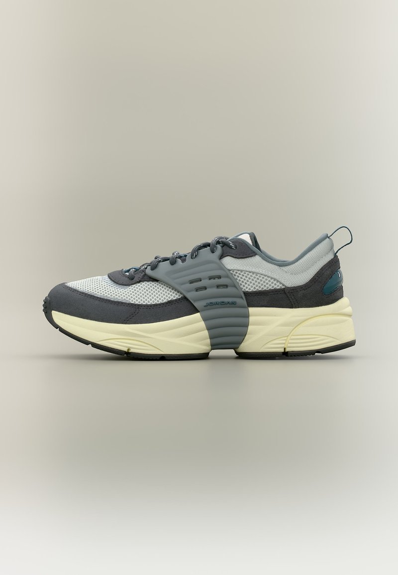 Παπούτσι τύπου Sneaker χαμηλού ύψους με γκρι διάτρητο υλικό και καστόρι, κρεμ ενδιάμεση σόλα, μαύρη εξωτερική σόλα και φαρδιά γκρι λωρίδα στο μέσο του ποδιού.