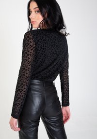 Black long-sleeve top with leopard print texture, sheer sleeves, paired with high-waisted black leather pants. Smooth and fitted design.