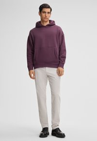Lila Kapuzenpullover mit einer Vordertasche, kombiniert mit hellen Hosen und schwarzen Schuhen. Glattes Material mit gerippten Bündchen und Saum.