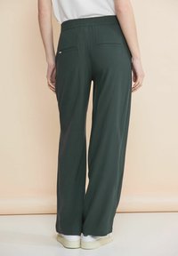 Gröna vida byxor med elastisk midja och två bakfickor. Materialet verkar mjukt och lätt, tillsammans med vita sneakers.