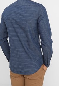 Marinblå långärmad skjorta med subtil prickig mönster, rundad nederkant och knappmanchetter. Tillverkad av lättviktsmaterial.